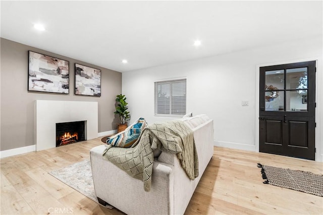 living area with recessed lighting, a warm lit fireplace, baseboards, and wood finished floors