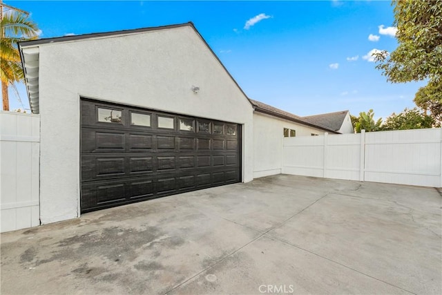 garage featuring concrete driveway and fence