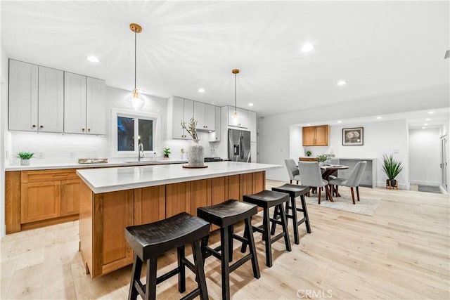 kitchen featuring a kitchen island, a sink, light countertops, light wood-style floors, and stainless steel fridge