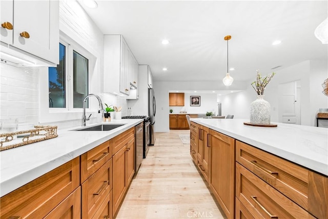 kitchen with light wood-type flooring, light countertops, brown cabinets, white cabinetry, and a sink