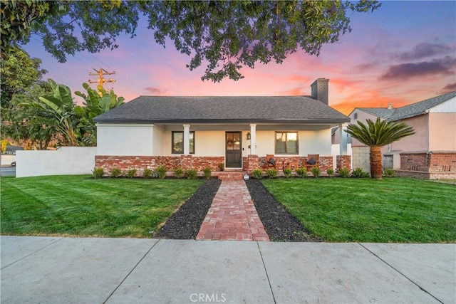 view of front of home featuring brick siding, stucco siding, a chimney, and a yard