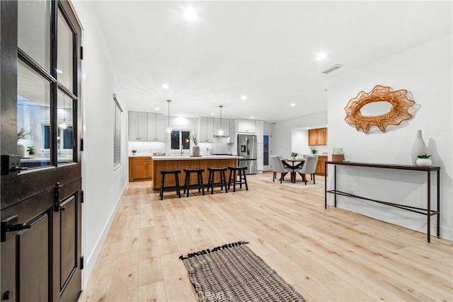 interior space with visible vents, a breakfast bar area, stainless steel fridge with ice dispenser, and light wood finished floors