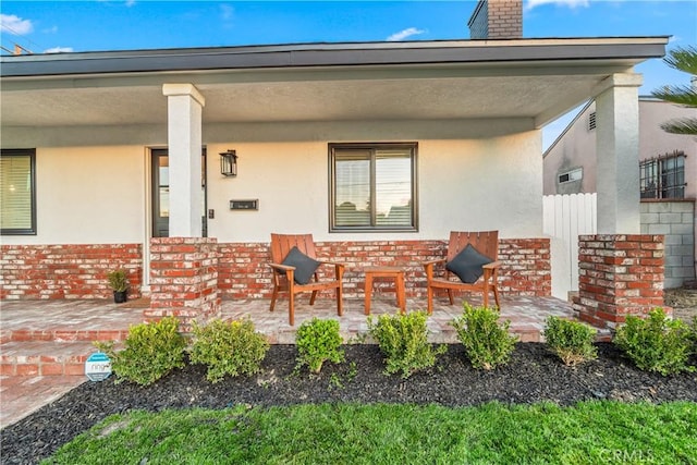 exterior space with stucco siding, brick siding, covered porch, and a chimney