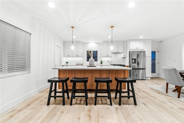 kitchen with light wood-style flooring, stainless steel fridge with ice dispenser, light countertops, pendant lighting, and a center island