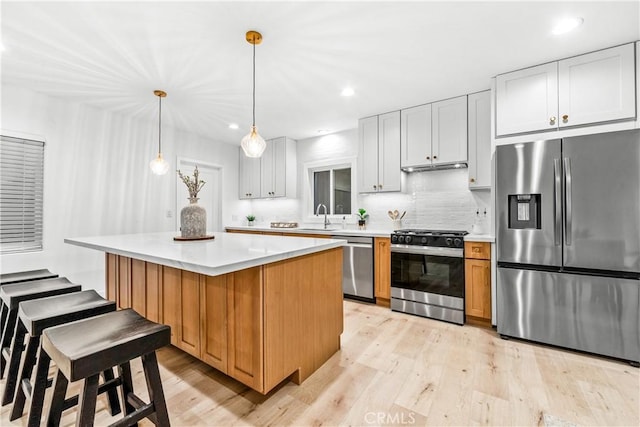 kitchen with appliances with stainless steel finishes, a kitchen island, light countertops, and light wood-style floors