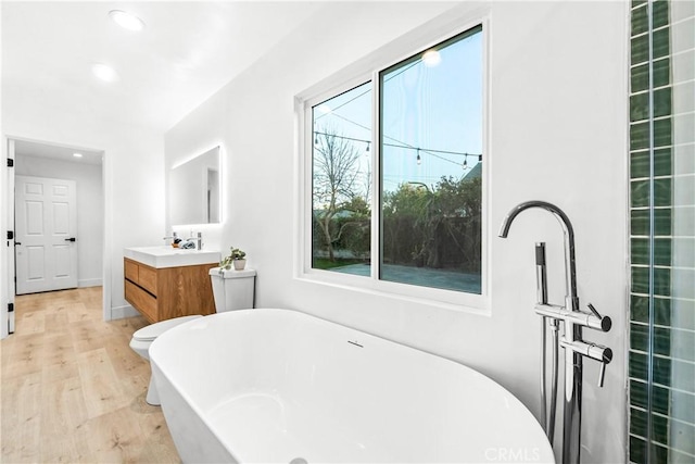 bathroom featuring vanity, a freestanding tub, recessed lighting, and wood finished floors