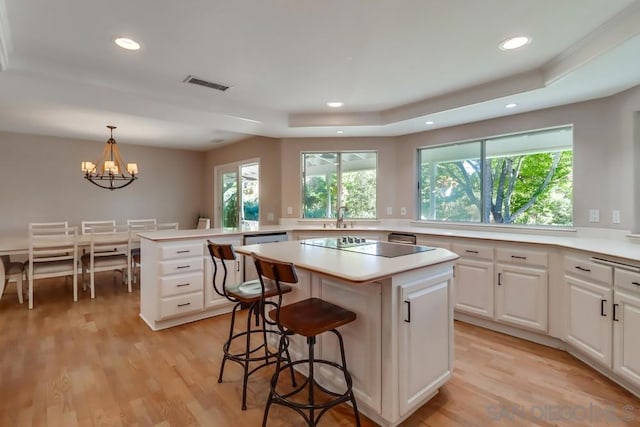 kitchen featuring a center island, white cabinets, decorative light fixtures, light hardwood / wood-style flooring, and a tray ceiling