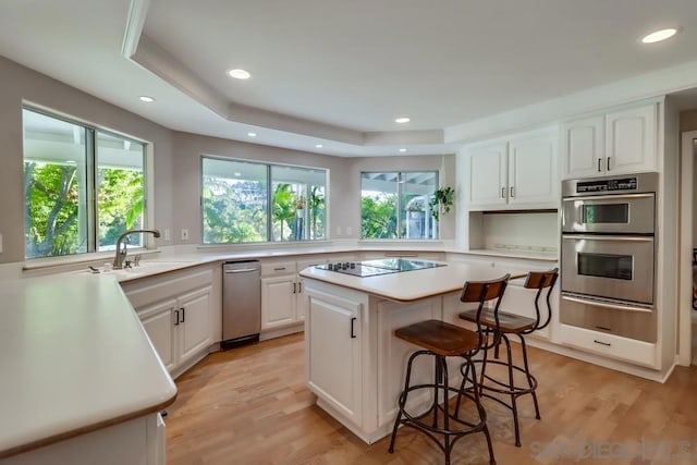 kitchen featuring black electric stovetop, white cabinets, a kitchen island, double oven, and a tray ceiling