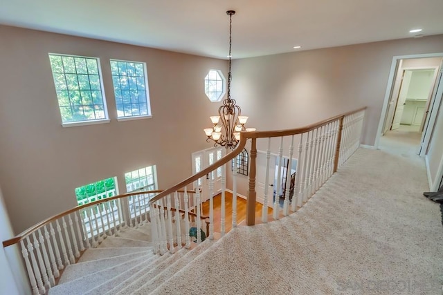 stairway featuring plenty of natural light, carpet, and a notable chandelier