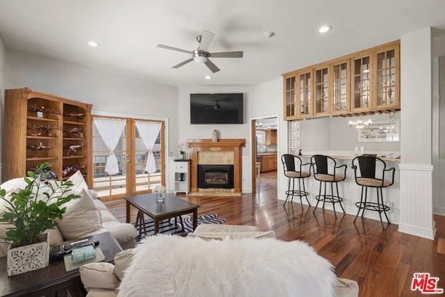 living room with a tiled fireplace, dark wood-type flooring, and ceiling fan