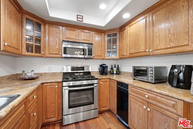 kitchen with light stone countertops, stainless steel appliances, sink, and light wood-type flooring