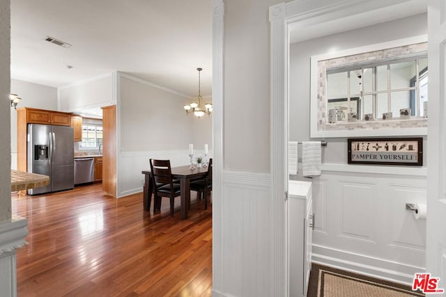 interior space with hardwood / wood-style flooring, ornamental molding, stainless steel appliances, and an inviting chandelier