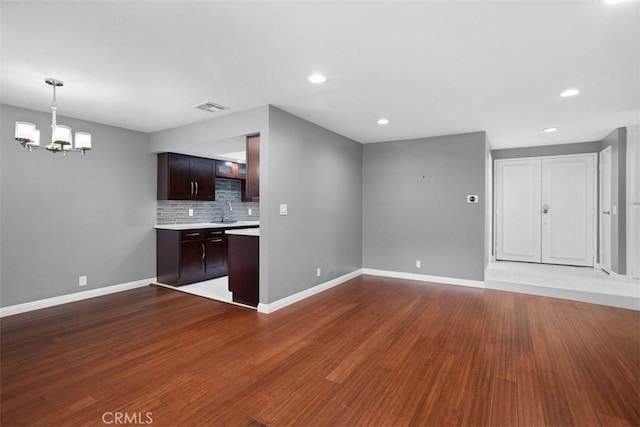 kitchen featuring a notable chandelier, decorative backsplash, sink, dark brown cabinetry, and dark hardwood / wood-style flooring