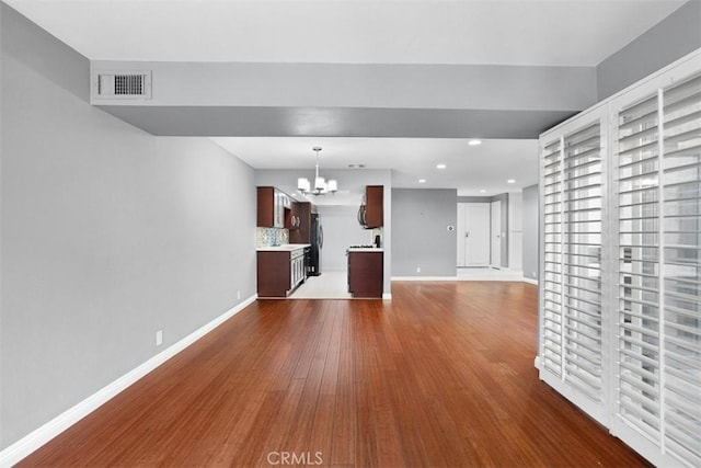 unfurnished living room with wood-type flooring and an inviting chandelier