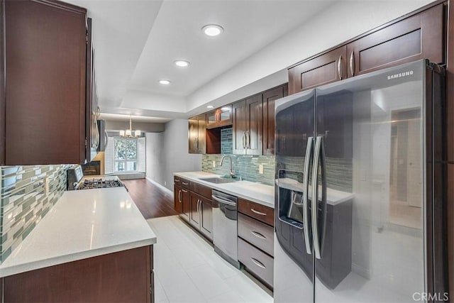 kitchen with appliances with stainless steel finishes, decorative light fixtures, decorative backsplash, sink, and a notable chandelier