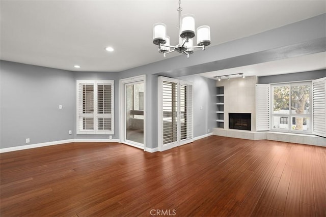 unfurnished living room featuring hardwood / wood-style flooring, a large fireplace, a chandelier, and a healthy amount of sunlight