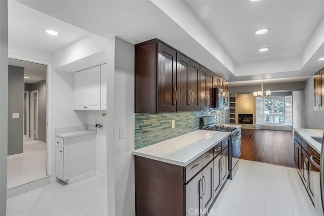 kitchen with a raised ceiling, appliances with stainless steel finishes, backsplash, light tile patterned floors, and dark brown cabinetry