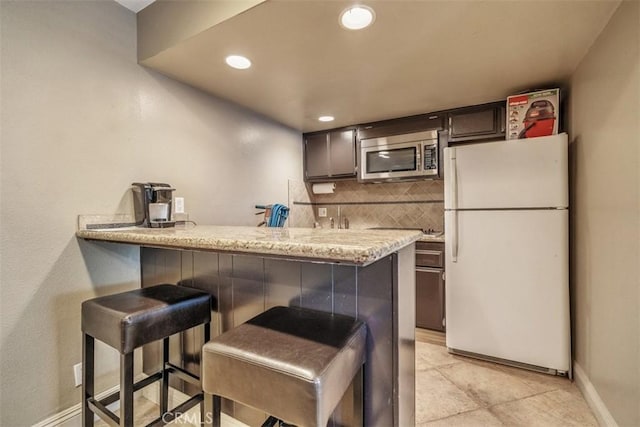 kitchen with backsplash, kitchen peninsula, white fridge, and a kitchen breakfast bar