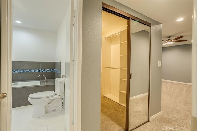 bathroom featuring toilet, a relaxing tiled tub, ceiling fan, and tile patterned floors