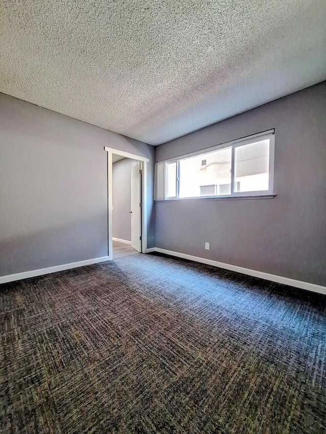 spare room featuring a textured ceiling and dark carpet