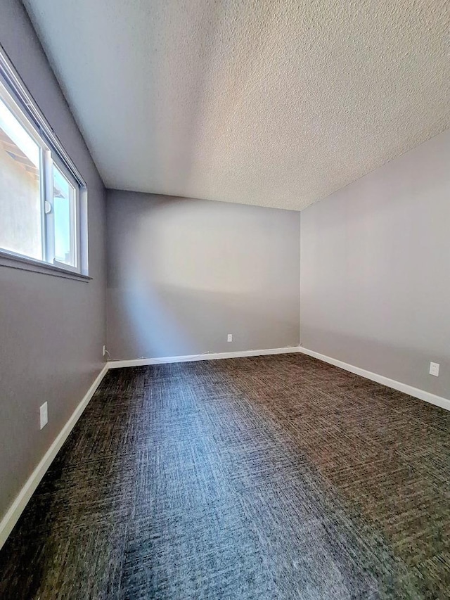 unfurnished room with dark carpet and a textured ceiling