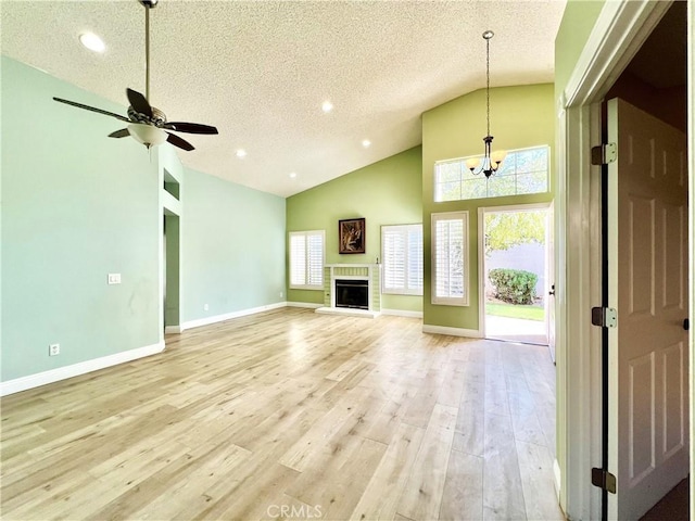 unfurnished living room featuring ceiling fan with notable chandelier, light hardwood / wood-style flooring, high vaulted ceiling, and a textured ceiling