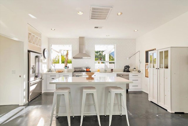 kitchen with white cabinets, a kitchen island, sink, wall chimney exhaust hood, and high quality appliances