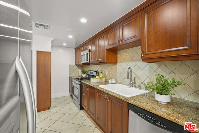 kitchen with appliances with stainless steel finishes, sink, backsplash, light stone counters, and light tile patterned flooring