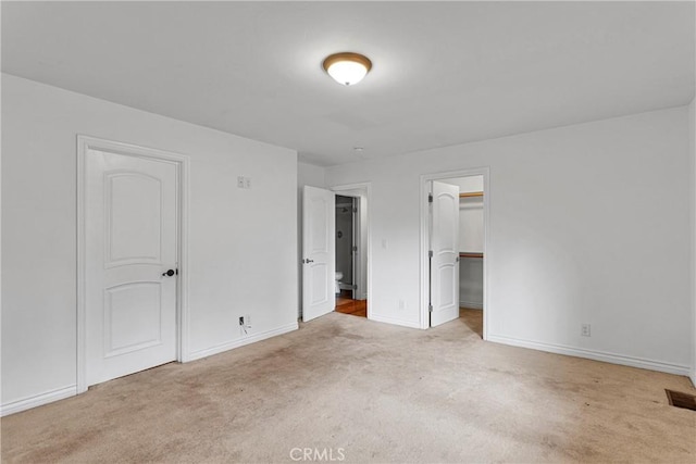 unfurnished bedroom featuring light colored carpet, a closet, and a spacious closet