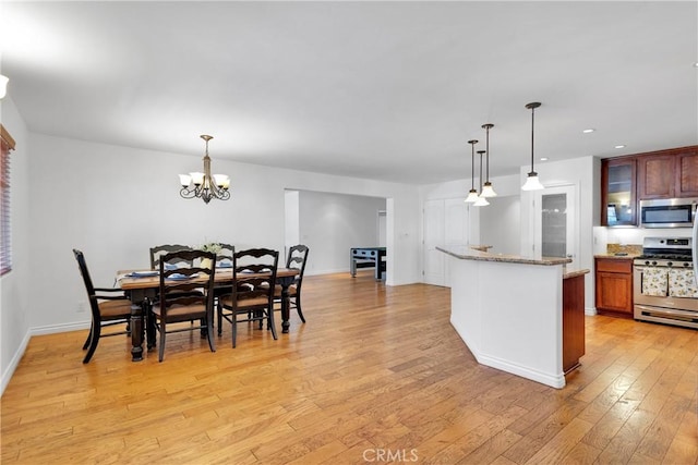 kitchen with decorative light fixtures, light stone counters, appliances with stainless steel finishes, and light hardwood / wood-style flooring