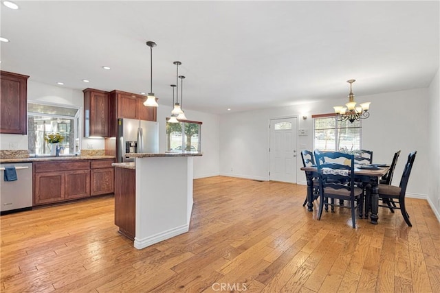 kitchen featuring light stone counters, light hardwood / wood-style flooring, hanging light fixtures, and appliances with stainless steel finishes