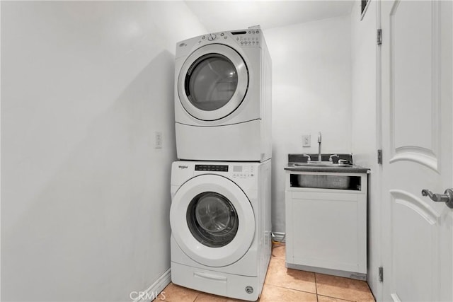 clothes washing area featuring stacked washer / dryer, light tile patterned flooring, and cabinets