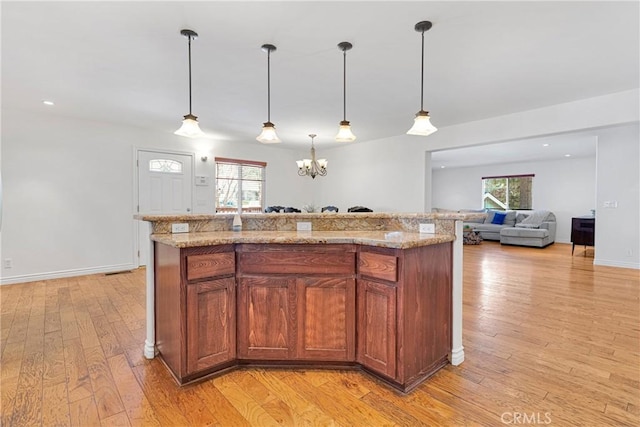 kitchen featuring a center island, light stone countertops, hanging light fixtures, light wood-type flooring, and an inviting chandelier