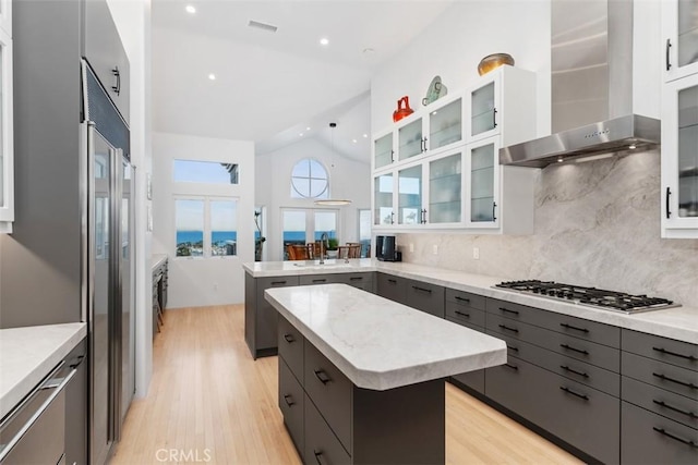 kitchen with vaulted ceiling, wall chimney exhaust hood, sink, a kitchen island, and decorative backsplash