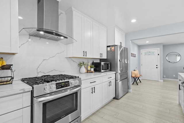 kitchen featuring stainless steel appliances, white cabinetry, wall chimney range hood, and light stone counters