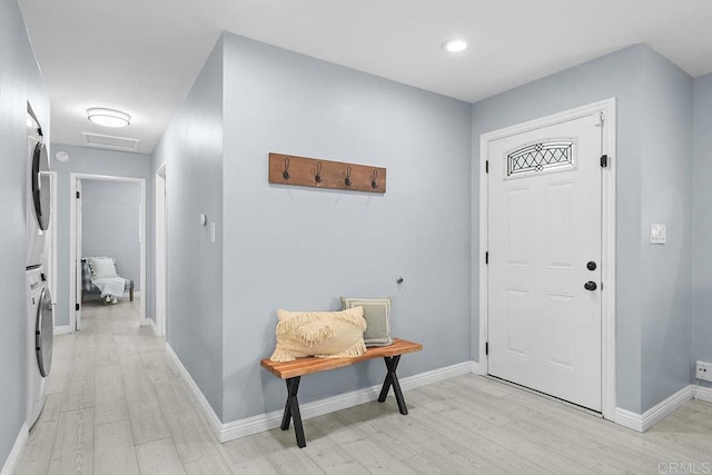 foyer with stacked washer / drying machine and light hardwood / wood-style flooring