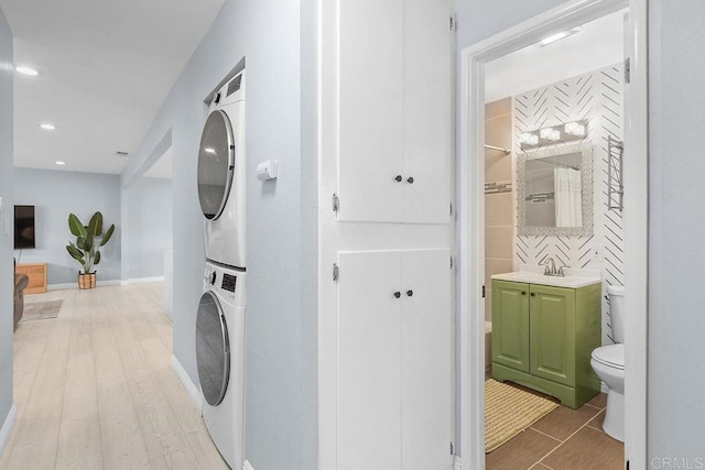 clothes washing area with stacked washer and dryer, sink, and light hardwood / wood-style flooring