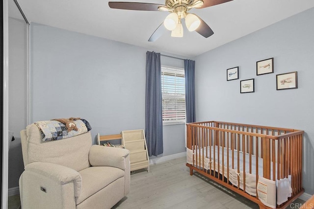 bedroom with a crib, ceiling fan, and light hardwood / wood-style flooring