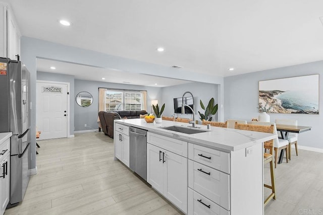 kitchen with a kitchen bar, sink, white cabinetry, appliances with stainless steel finishes, and an island with sink