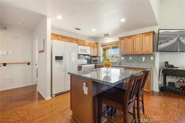 kitchen with dark stone countertops, a center island, white appliances, and light hardwood / wood-style flooring