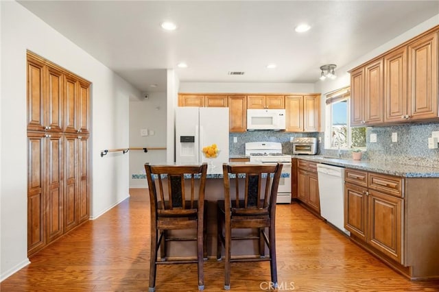 kitchen with a center island, white appliances, a kitchen breakfast bar, light hardwood / wood-style flooring, and light stone counters