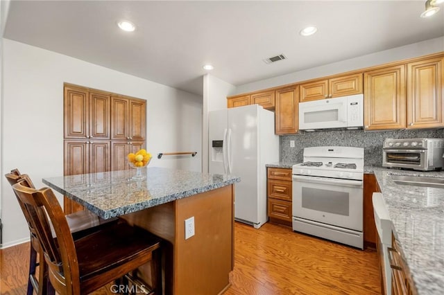 kitchen featuring light stone countertops, a breakfast bar, white appliances, and backsplash