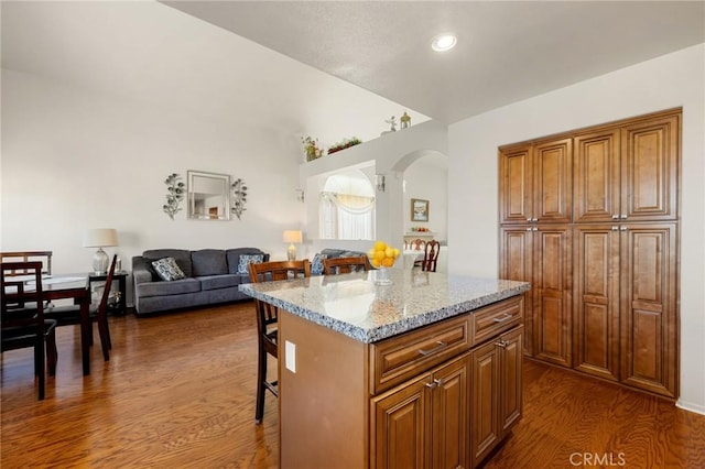 kitchen featuring a kitchen island, light stone counters, dark hardwood / wood-style flooring, and a kitchen breakfast bar