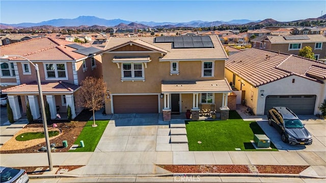 view of front of home with a garage, a mountain view, solar panels, and a front yard