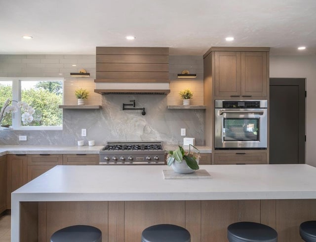 kitchen with wall chimney exhaust hood, stainless steel oven, tasteful backsplash, and range