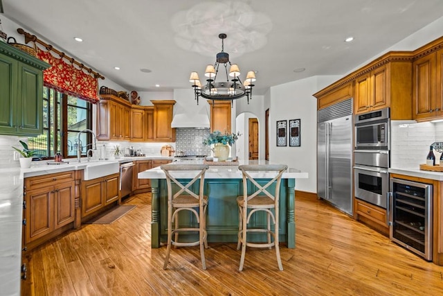 kitchen featuring beverage cooler, custom exhaust hood, a kitchen island, stainless steel appliances, and a breakfast bar area