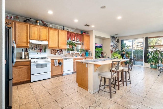 kitchen featuring a kitchen island, light tile patterned flooring, white appliances, and a breakfast bar