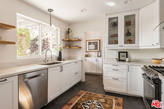 kitchen with appliances with stainless steel finishes, pendant lighting, sink, white cabinets, and wall chimney exhaust hood