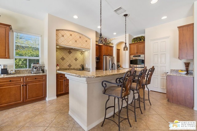 kitchen featuring stainless steel appliances, decorative backsplash, hanging light fixtures, a kitchen island with sink, and a breakfast bar