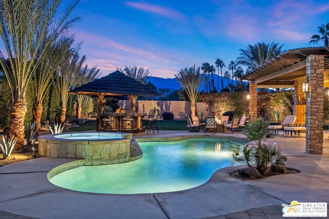 pool at dusk featuring an in ground hot tub, a patio area, exterior bar, and a mountain view